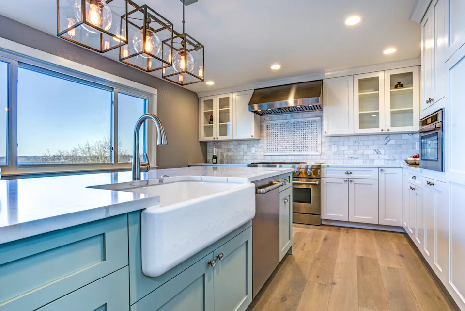 Modern kitchen with farmhouse sink, stainless steel appliances, and pendant lights over island. Large window provides natural light