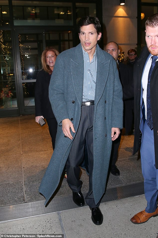 He wore a gray coat layered over a blue button-up shirt, which he tucked into charcoal gray trousers