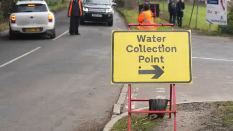 Eddie Mitchell A yellow and black road sign directing drivers to a water collection point at East Grinstead Rugby Club.