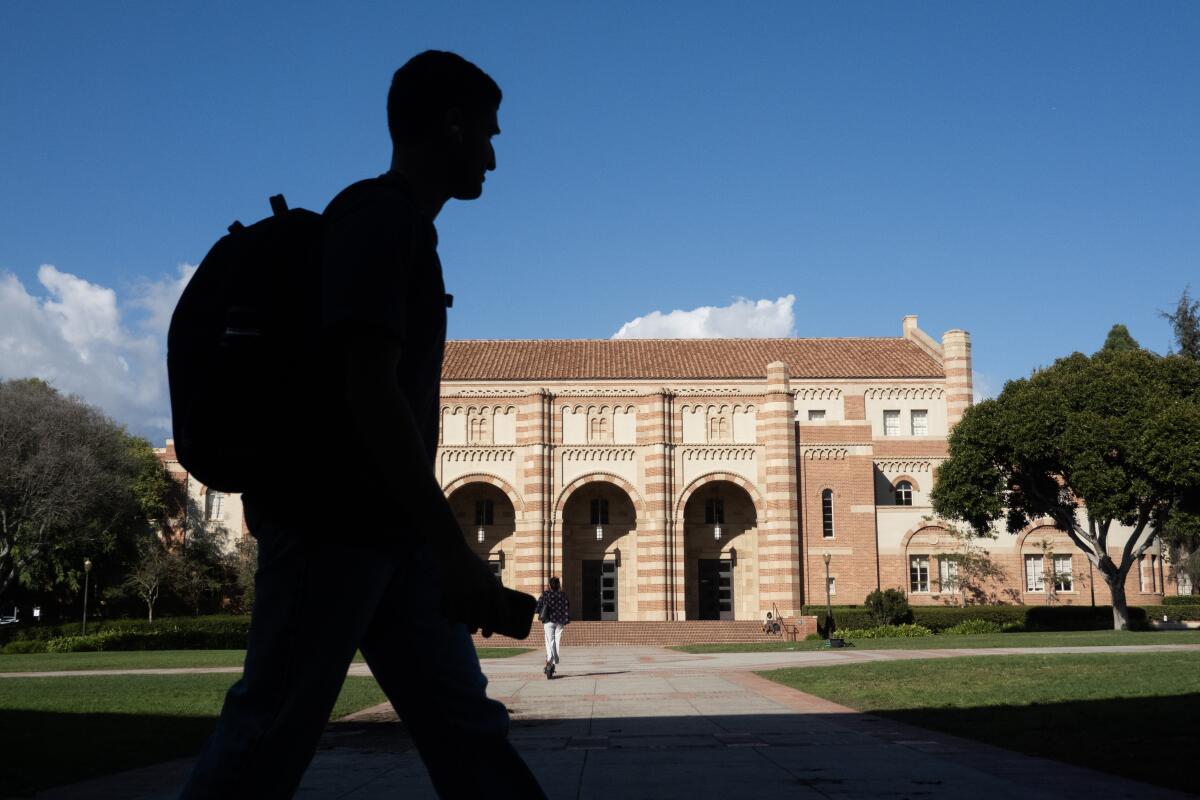 A man with a backpack, seen in silhouette, walks in front of a brick building with arches