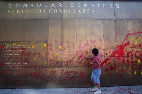 A woman defaces the facade of the U.S. Embassy with red handprints in protest against the capture of President Nicolas Maduro, in Mexico City, Saturday, Jan. 3, 2026. (AP Photo/Marco Ugarte)