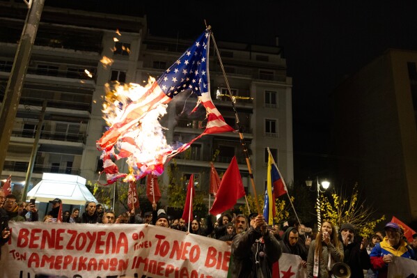 A protester raises a US flag which has been set ablaze during a rally opposing the United States strikes on Venezuela and the capturing of its President Nicolas Maduro, outside the U.S embassy in Athens, Greece, Saturday, Jan. 3, 2026. (AP Photo/Yorgos Karahalis)