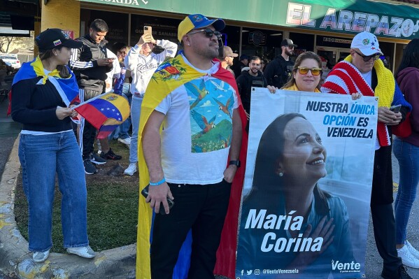 From left, Venezuelans David Nuñez, Lisbeth Garcia, Victor Gimenez gather outside El Arepazo restaurant with a banner of opposition leader and Nobel Peace Prize winner Maria Corina Machado amid celebrations following news of Venezuelan President Nicolás Maduro capture in Doral, Fla., on Saturday, Jan. 3, 2026. (AP Photo/Vanessa Alvarez)