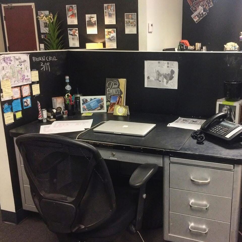 A desk is seen in an office. The desk is black with silver cabinets. A black desk chair sits underneath part of the desk. There is a computer on top of the desk. The desk has various post-it notes and papers taped to its walls.