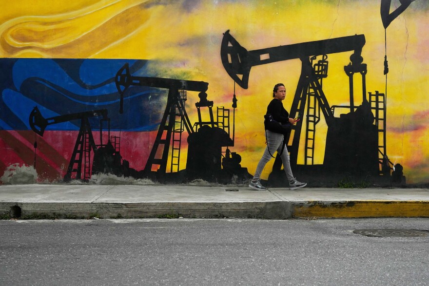 A person walks on a sidewalk in front of a colorful mural depicting oil pumpjacks silhouetted against a yellow, blue, and red background.