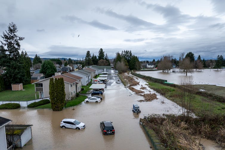 Water fills a street over the wheels of cars next to a river.