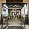 This photo shows the double glass doors of the Medically Vulnerable People shelter in Sandy, Utah. The building's exterior walls are brown bricks. Above the glass doors are the words "WELCOME TO THE MVP PROGRAM."