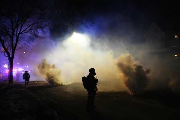 Law enforcement officers stand amid tear gas at the scene of a reported shooting Wednesday, Jan. 14, 2026, in Minneapolis. (AP Photo/Adam Gray)