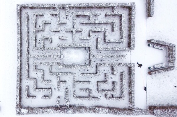 A man walks his dog past a snow-covered labyrinth at a castle garden in Gelsenkirchen, Germany, Saturday, Jan. 10, 2026. (AP Photo/Martin Meissner)