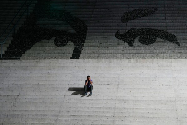 A man sits on steps decorated with a mural representing the eyes of late Venezuelan President Hugo Chavez in Caracas, Venezuela, Monday, Jan. 12, 2026. (AP Photo/Matias Delacroix)