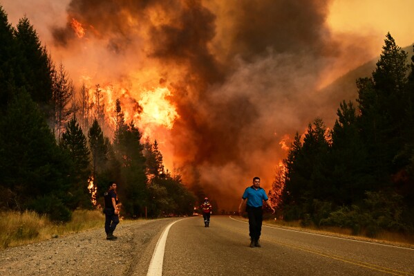 People walk on a road as a wildfire blazes in El Hoyo, Patagonia, Argentina, Thursday, Jan. 8, 2026. (AP Photo/Maxi Jonas)