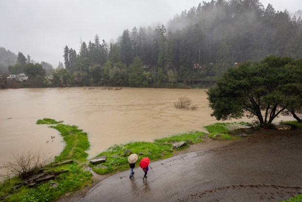 Locals find a break in the rain to have a walk and check the level of the Russian River Monday, Jan. 5, 2026 at the Monte Rio bridge. Sonoma Water is asking residents to stay away from the river after untreated wastewater spilled into the river. (John Burgess / The Press Democrat)