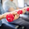 A closeup of a senior woman's forearm as she lifts a red hand weight. 