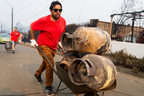 CORRECTS NAME TO VICTOR SILVA AND REMOVES ANDRES GARRIDO - Resident Victor Silva pushes a wheelbarrow with gas cylinders burned when wildfires destroyed homes in Tome, Chile, Monday, Jan. 19, 2026. (AP Photo/Javier Torres)