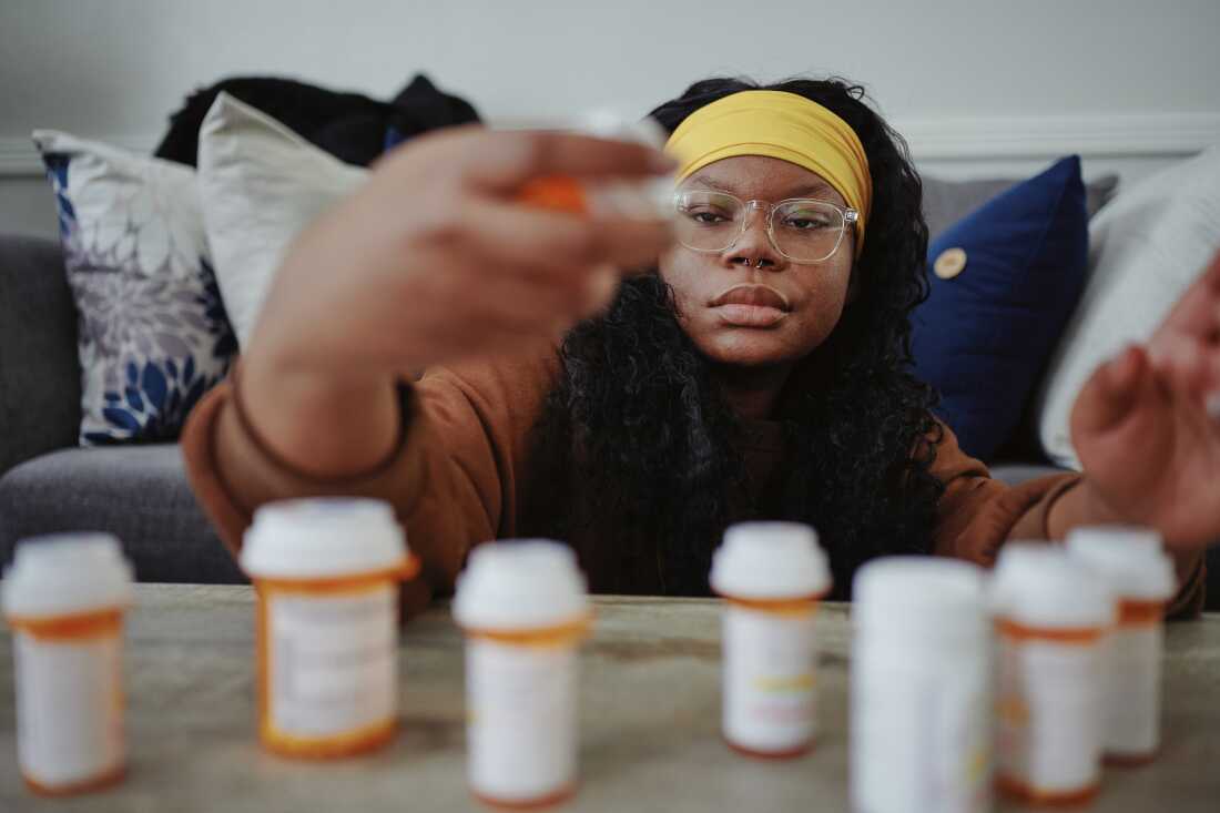 Serenity Cole is shown with many pill bottles arrayed on a table before her.