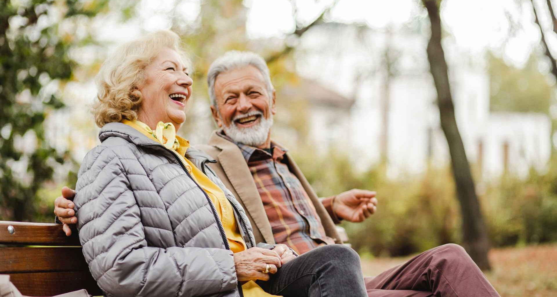 A happy senior couple sitting on a bench outside during winter weather together in warm clothing.
