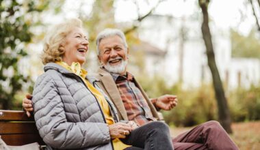 A happy senior couple sitting on a bench outside during winter weather together in warm clothing.