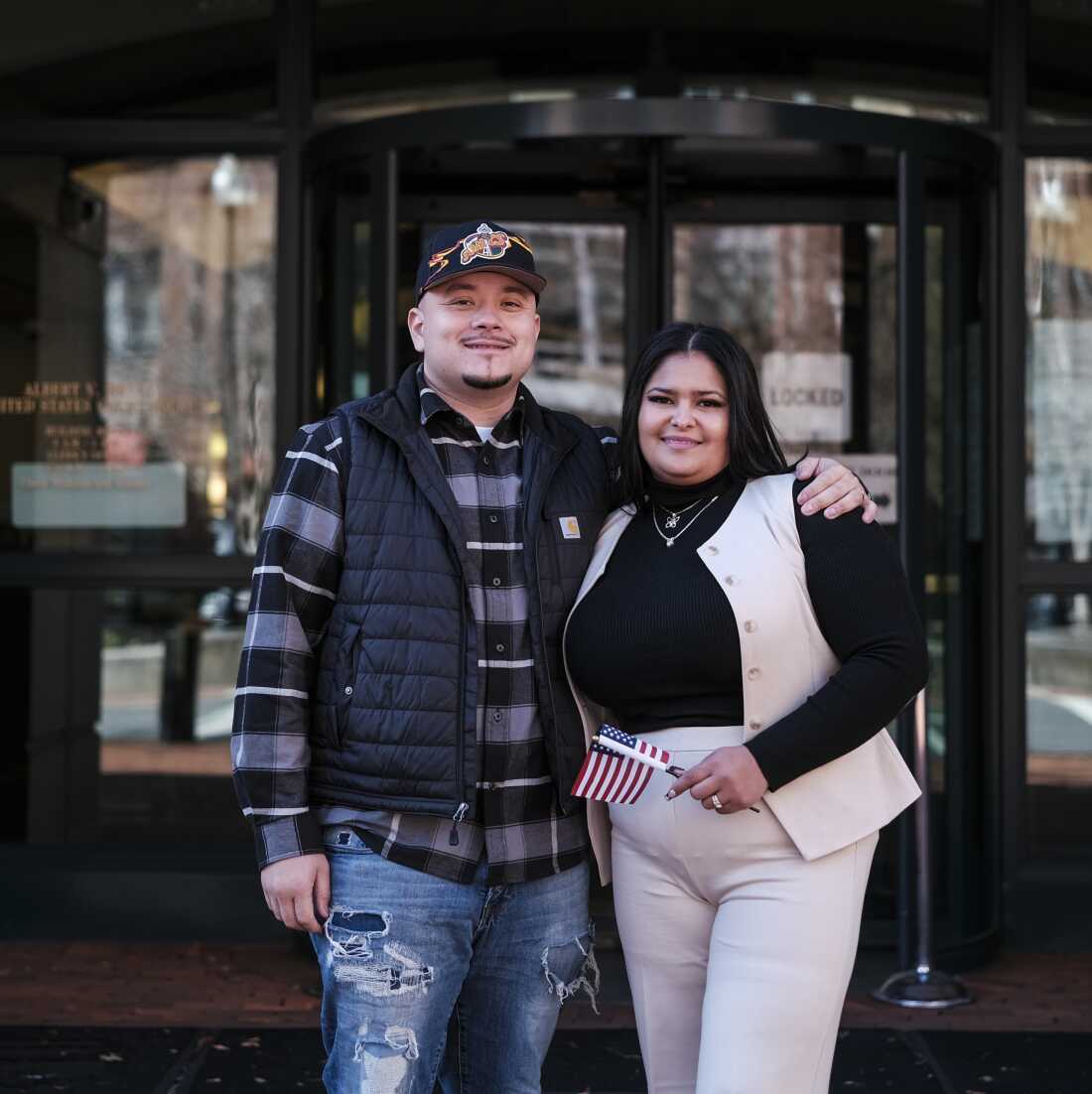 Ashley Lezama (right), of Honduras, holds a small American flag and stands with her husband, Nick Moreno, of Bolivia following her naturalization ceremony in Alexandria, Va.
