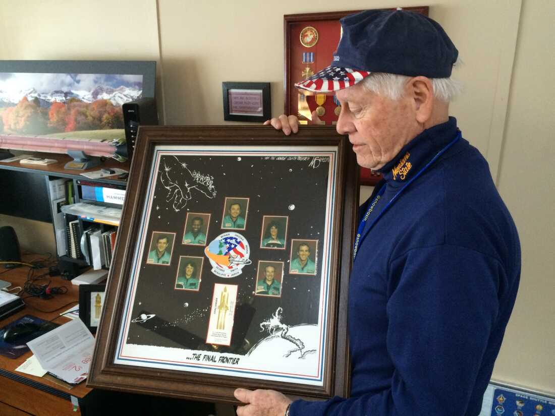 Allan McDonald in 2016 holds a framed commemorative poster honoring the seven astronauts killed aboard the space shuttle Challenger. The poster features headshots of the seven astronauts.