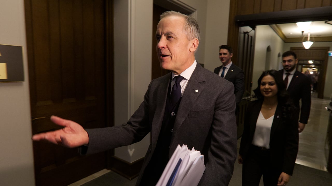A man in a suit walks in a hallway with some people behind him.