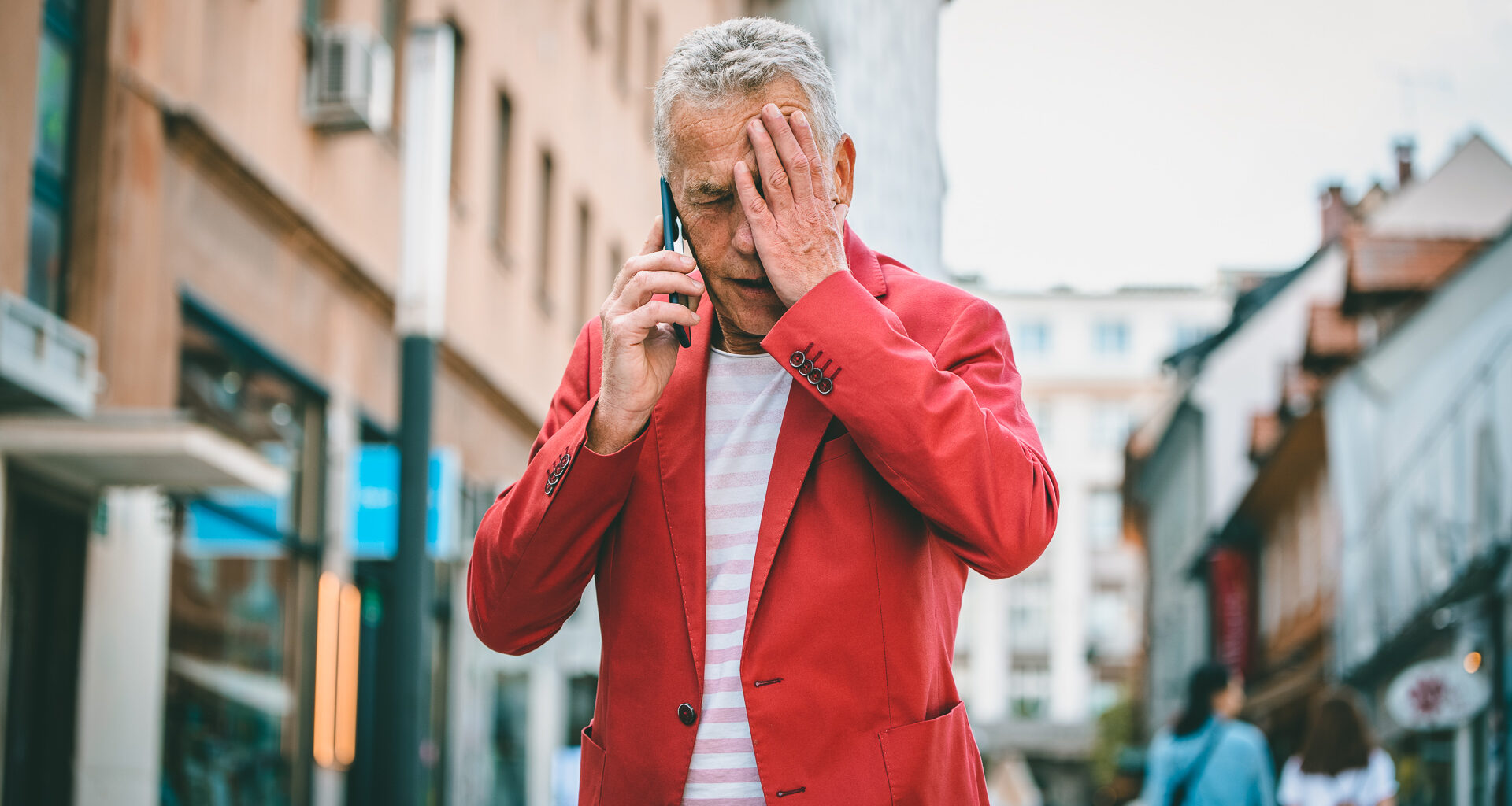 Low angle front view close-up of Caucasian man in early 60s learning bad news as he pauses to take an outdoor call during city break in Ljubljana.