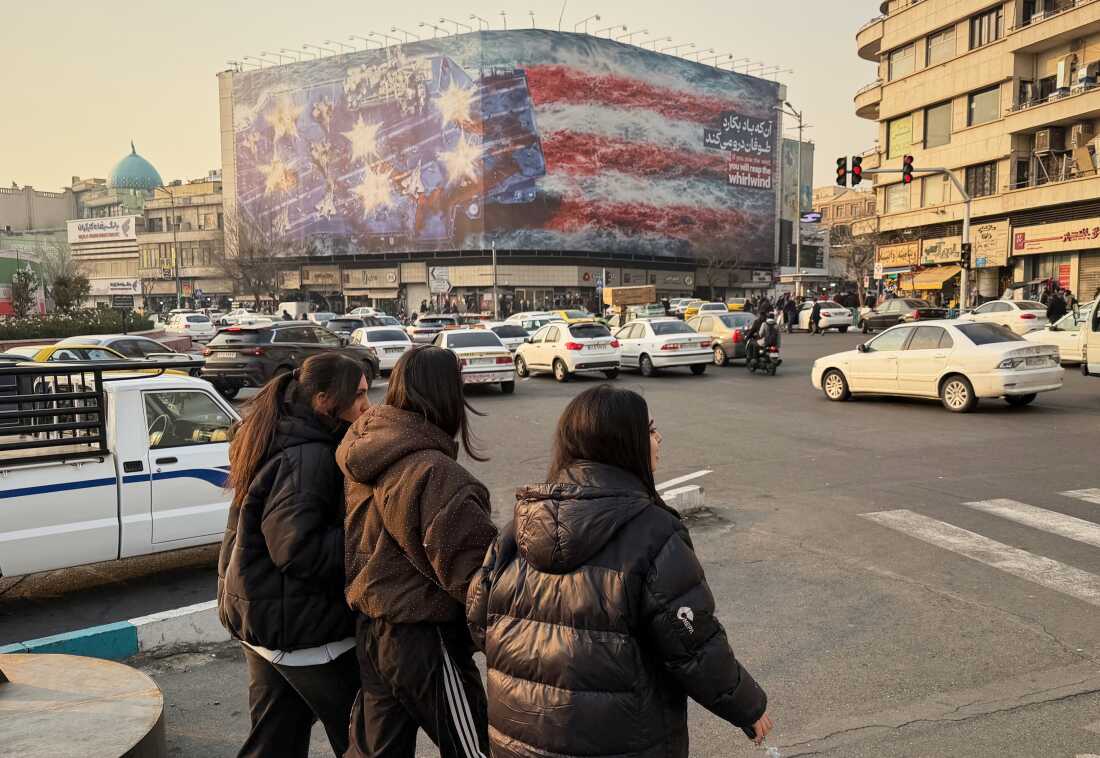 People walk in front a billboard with graphic showing a U.S aircraft carrier with damaged fighter jets on its deck, and sign reading in Farsi and English: "If you sow the wind, you'll reap whirlwind," at the Enqelab-e-Eslami (Islamic Revolution) square, in Tehran, Iran, Sunday, Jan. 25, 2026.
