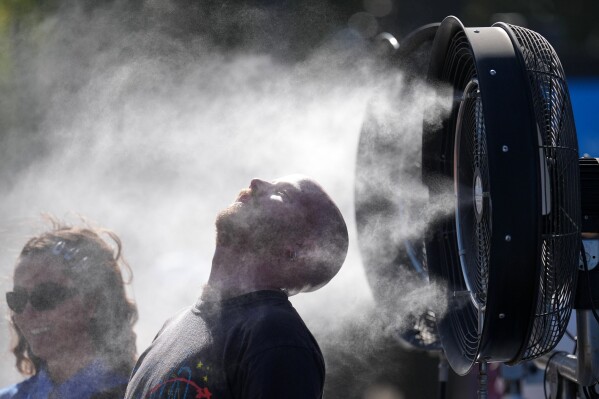Spectators cool down at water mister machines at the Australian Open tennis championship in Melbourne, Australia, Saturday, Jan. 24, 2026. (AP Photo/Dita Alangkara)