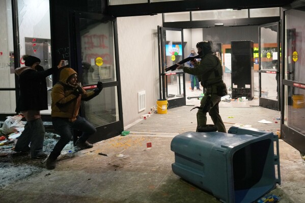 A federal agent points a weapon at a person outside a hotel during a noise demonstration protest in response to federal immigration enforcement operations in the city Sunday, Jan. 25, 2026, in Minneapolis. (AP Photo/Adam Gray, File)