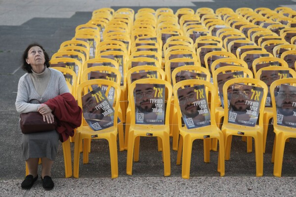 A woman sits for a moment by chairs with photos of Ran Gvili, the final hostage in Gaza who was killed while fighting Hamas militants during the Oct. 7, 2023 attack, on the same day his remains were recovered, in a plaza known as Hostages Square, in Tel Aviv, Israel, Monday, Jan. 26, 2026. (AP Photo/Oded Balilty, File)