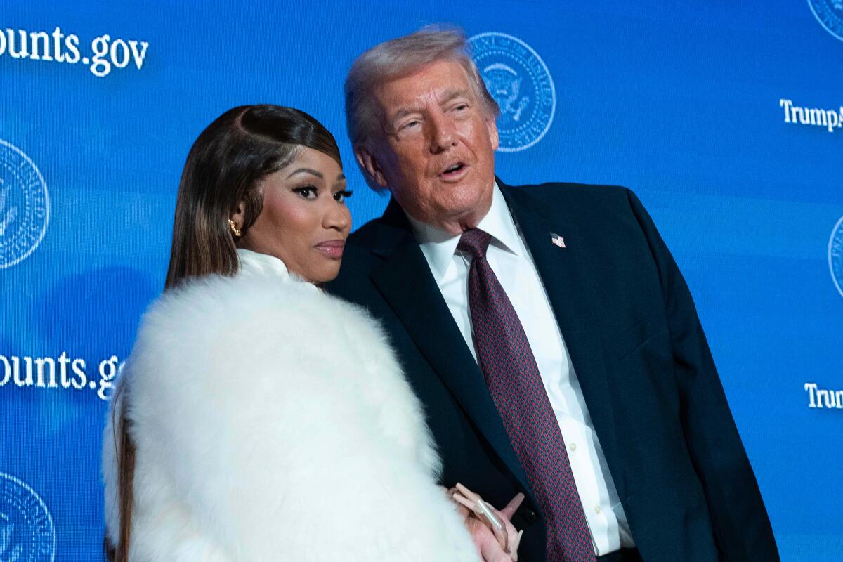 Nicki Minaj in a fluffy white jacket holding hands with and standing close to President Trump