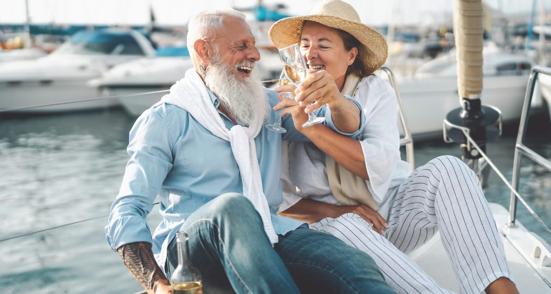 Senior couple toasting champagne on sailboat vacation - Happy elderly people having fun celebrating wedding anniversary on boat trip - Love relationship and travel lifestyle concept.