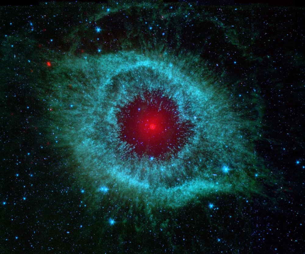 This infrared false-colour image of the Helix Nebula comes from the Spitzer Space Telescope. The white dwarf at the heart of the nebula appears red in this image, suggesting a malevolent eye. Image Credit: By NASA/JPL-Caltech/Univ. of Ariz. - NASA - Comets Kick up Dust in Helix Nebula, Public Domain, https://commons.wikimedia.org/w/index.php?curid=1669175