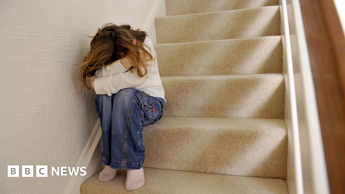 A generic picture of a girl sitting on a carpeted staircase in a home with their head in their hands. The girl is wearing jeans and white sweatshirt, she has long blonde hair but her face is obscured by her posture.