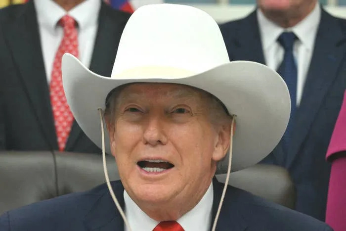 Person in a cowboy hat speaks at an event with people in suits and hats behind them