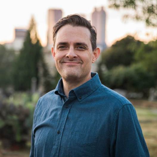 A man wearing a blue shirt standing in a park.