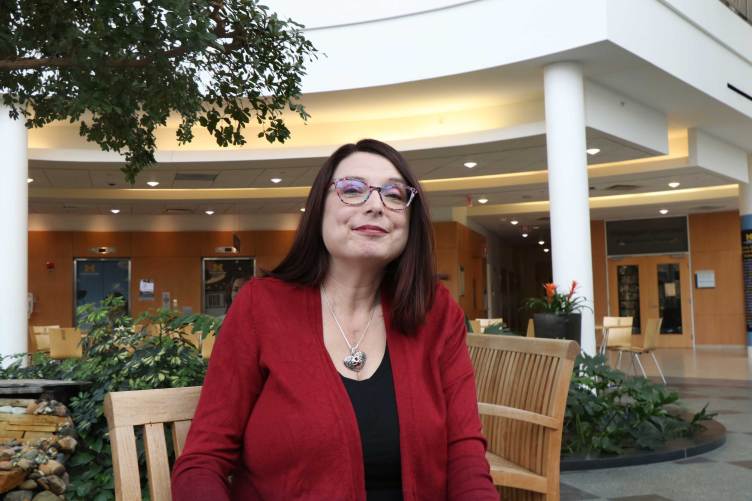 A woman wearing glasses sitting on a bench in an indoor atrium with plants.