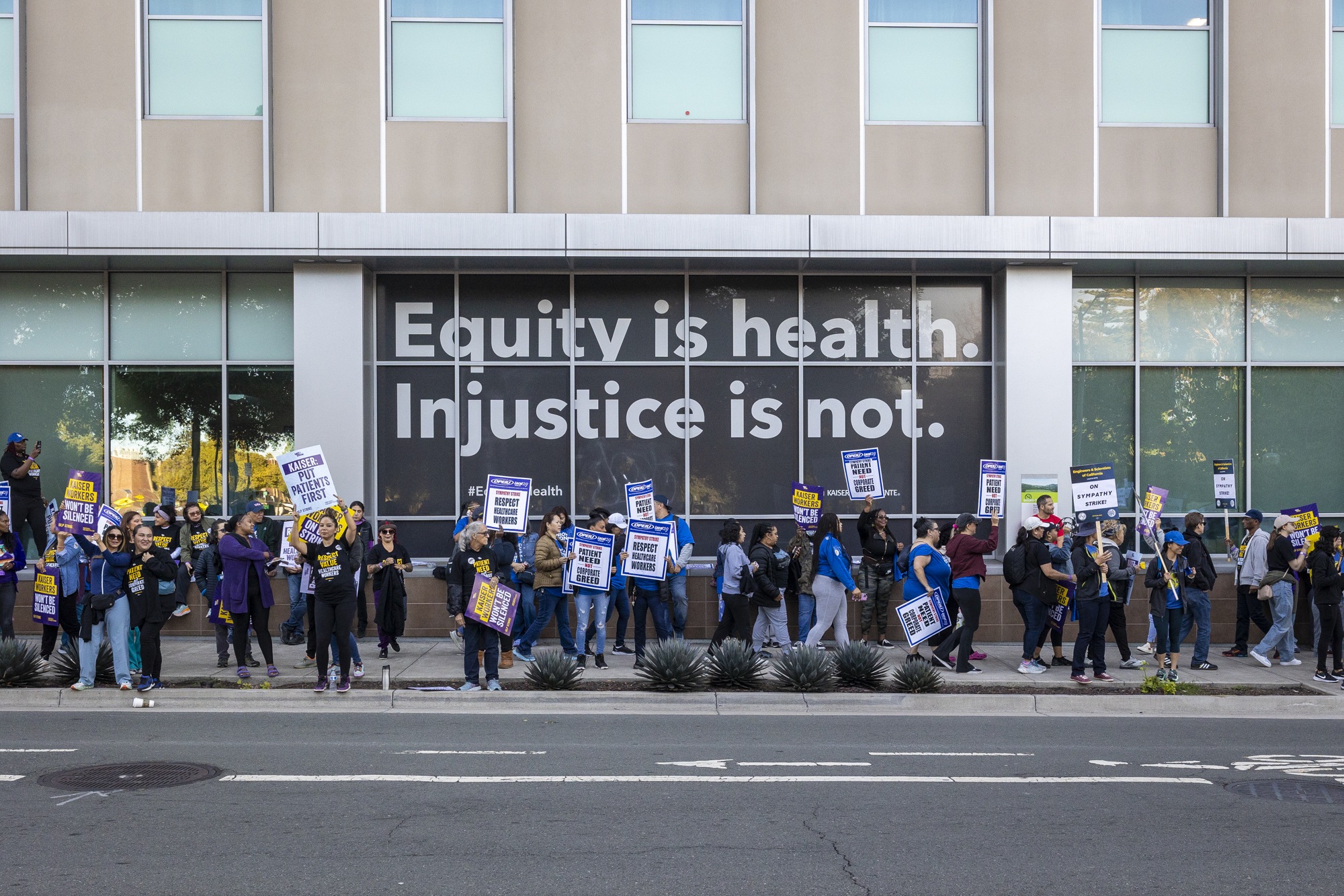 A large group of people line the sidewalk in front of a large building.