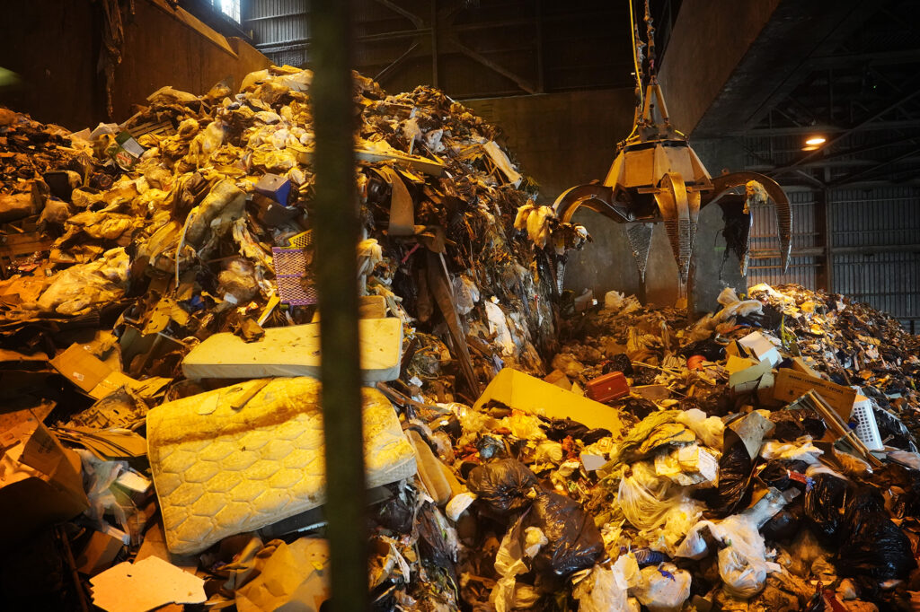 H-Power Supervisor Carl Krause operates the crane to move rubbish during a Tour de Trash visit Wednesday, Aug. 28, 2024, in Kapolei. The City and County of Honolulu’s Refuse Division hosts the tour which follows the journey of Oahu residents and visitors’ rubbish, recyclable items and compostable/green waste take through the collection and disposal process. (Kevin Fujii/Civil Beat/2024)
