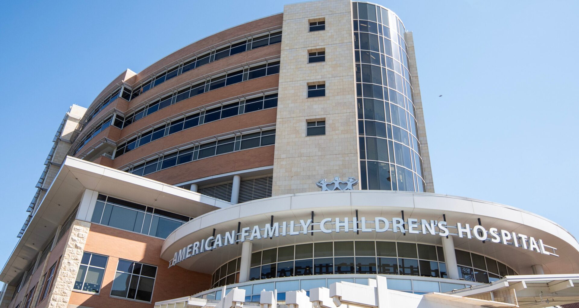 A modern multi-story building with glass and stone features, displaying the sign American Family Childrens Hospital under a clear blue sky.