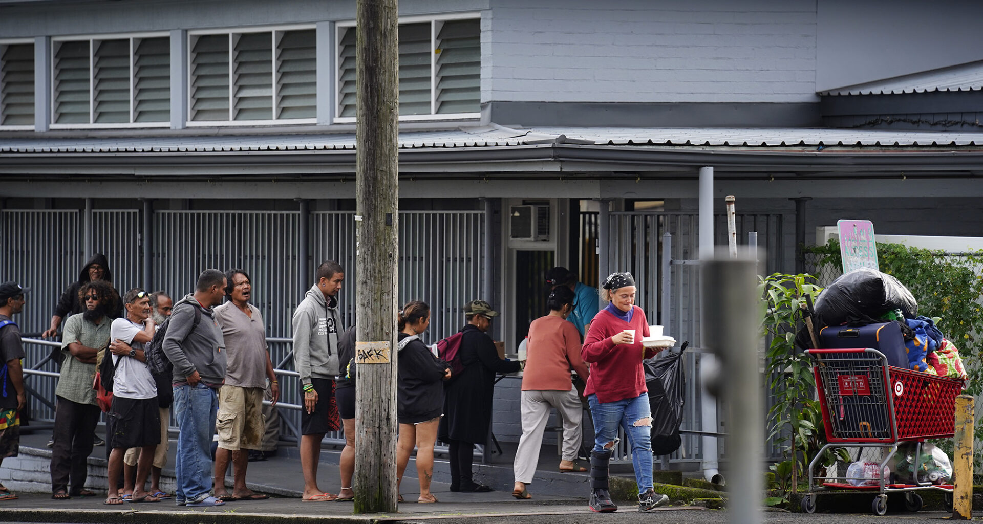 People line up for a meal from the Salvation Army Tuesday, Dec. 16, 2025, in Hilo. Lincoln Park sits across the street where many homeless have taken up residence. (Kevin Fujii/Civil Beat/2025)