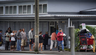 People line up for a meal from the Salvation Army Tuesday, Dec. 16, 2025, in Hilo. Lincoln Park sits across the street where many homeless have taken up residence. (Kevin Fujii/Civil Beat/2025)