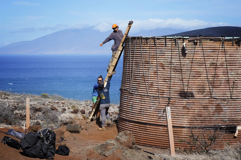 Protect Kahoʻolawe ʻOhana (PKO) Kawai Lu‘uwai, from top, Kaipu Keala and Kaulu Lu‘uwai move the remaining tarp on their catchment water tank Tuesday, Jan. 6, 2026, in Hakioawa. The tank’s second tarp was damaged and removed. (Kevin Fujii/Civil Beat/2026)