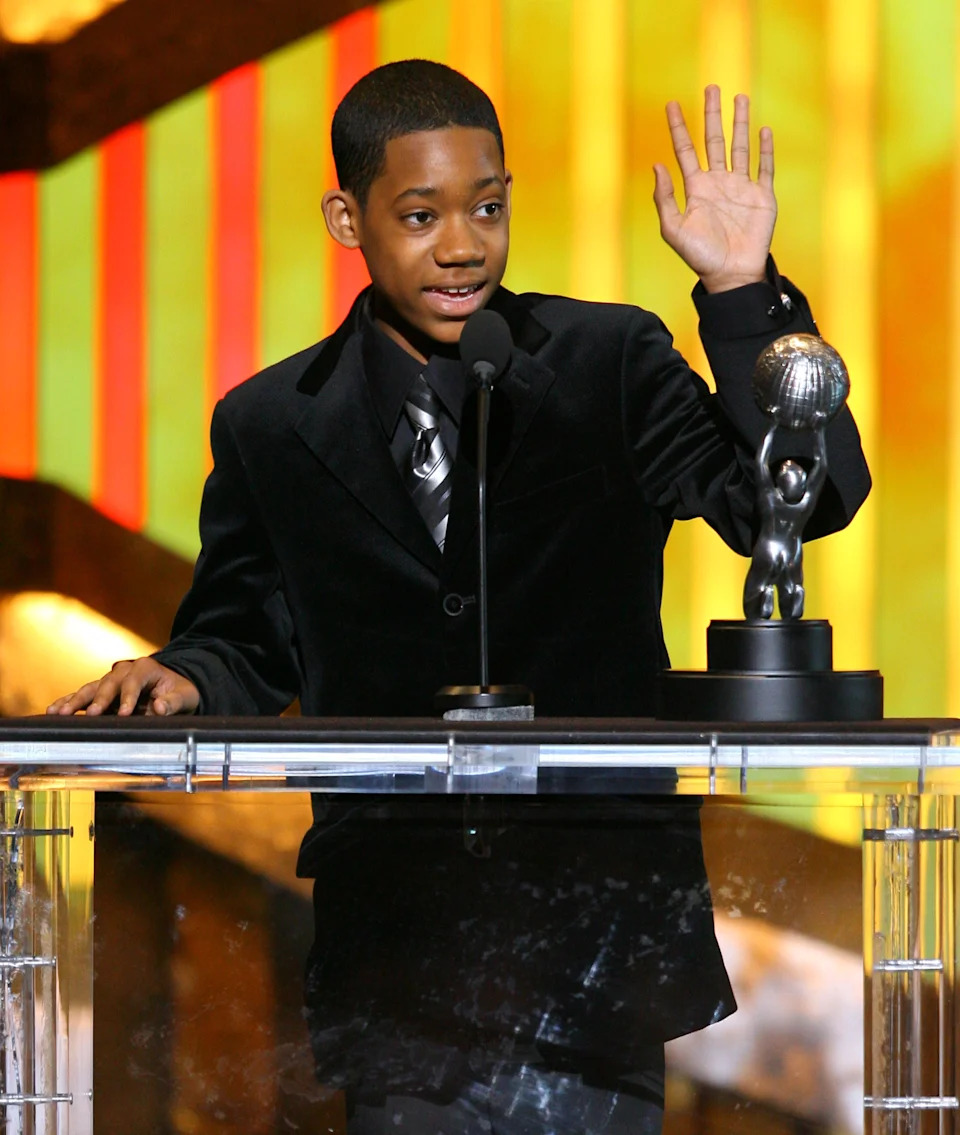 Young Tyler standing at a podium with an award trophy nearby