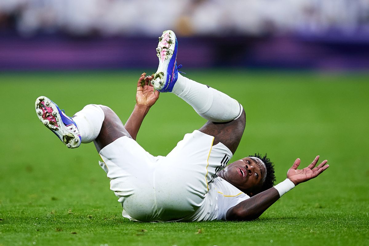 Vinicius Junior in Real Madrid home colours rolls around on the pitch.