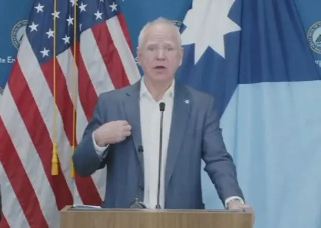 Minnesota Governor Tim Walz gestures toward himself while speaking at a media conference