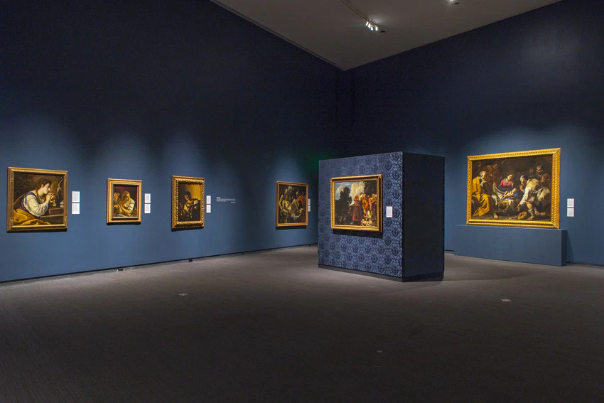 Art gallery interior displaying framed classical paintings on dark blue walls.