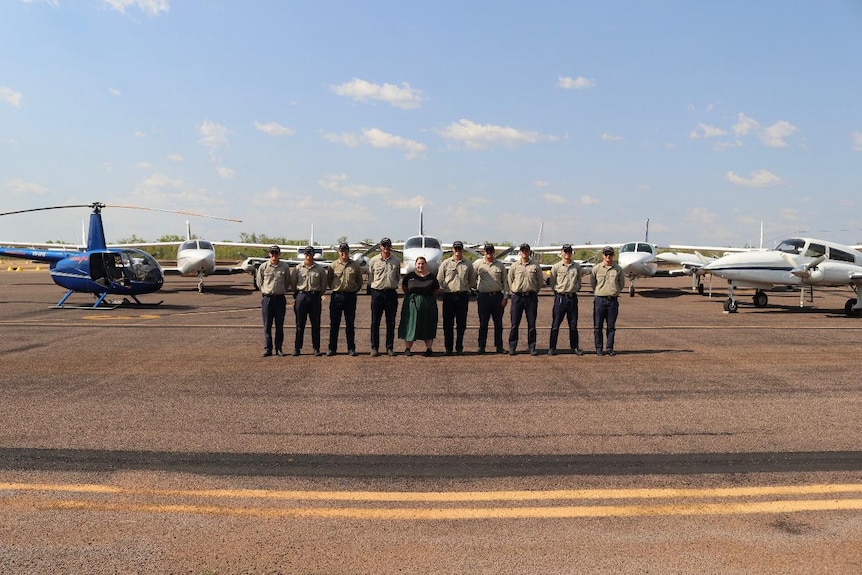 A group of people in uniform lined up in front of planes on an airstrip