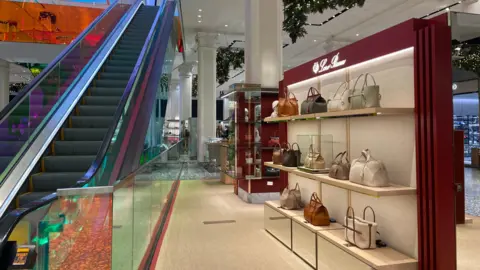 Danielle Kaye/BBC Bags are showcased next to as escalator in a department store.