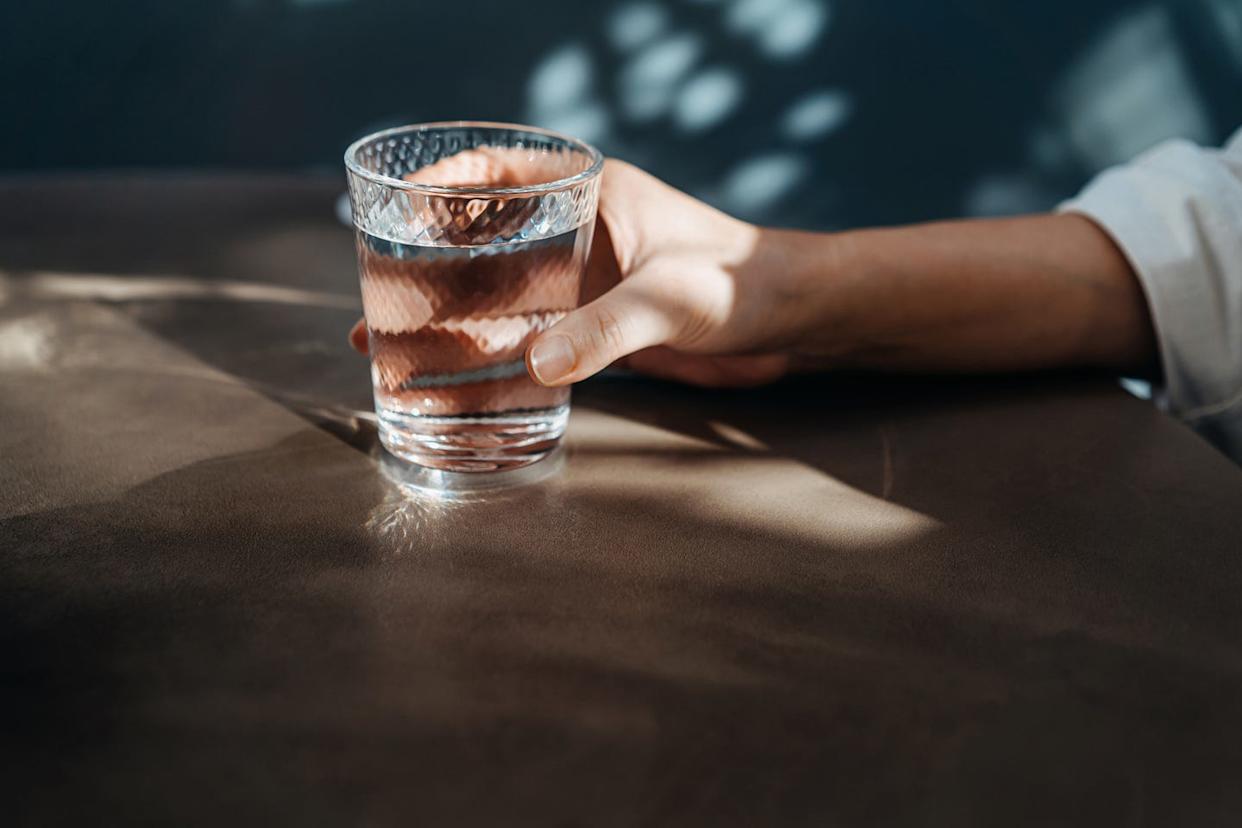 close up shot of a young asian woman drinking a glass of water while sitting in dining table in restaurant. female hand holding a glass of water. healthy lifestyle. staying hydrated