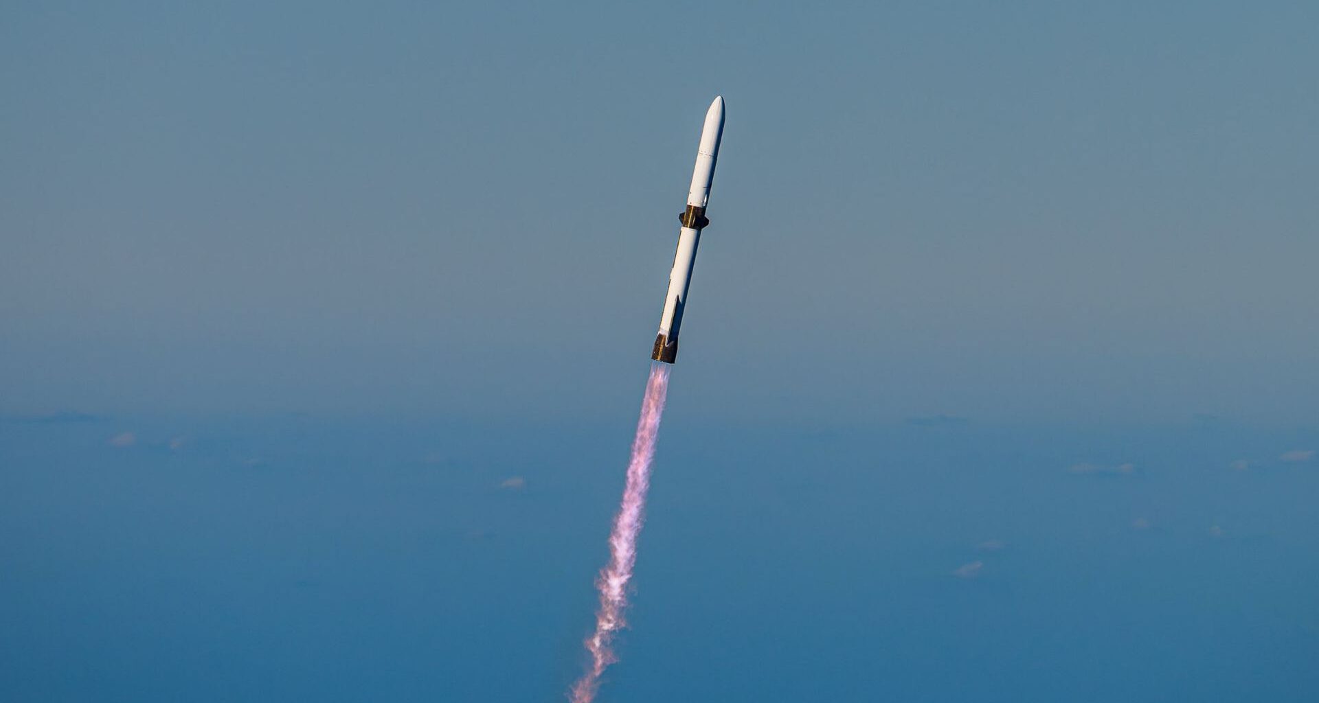 a white rocket climbs into a clear blue sky